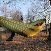 Person relaxing in a dark olive Bushmen ULTRALIGHT Hammock in a natural outdoor setting.